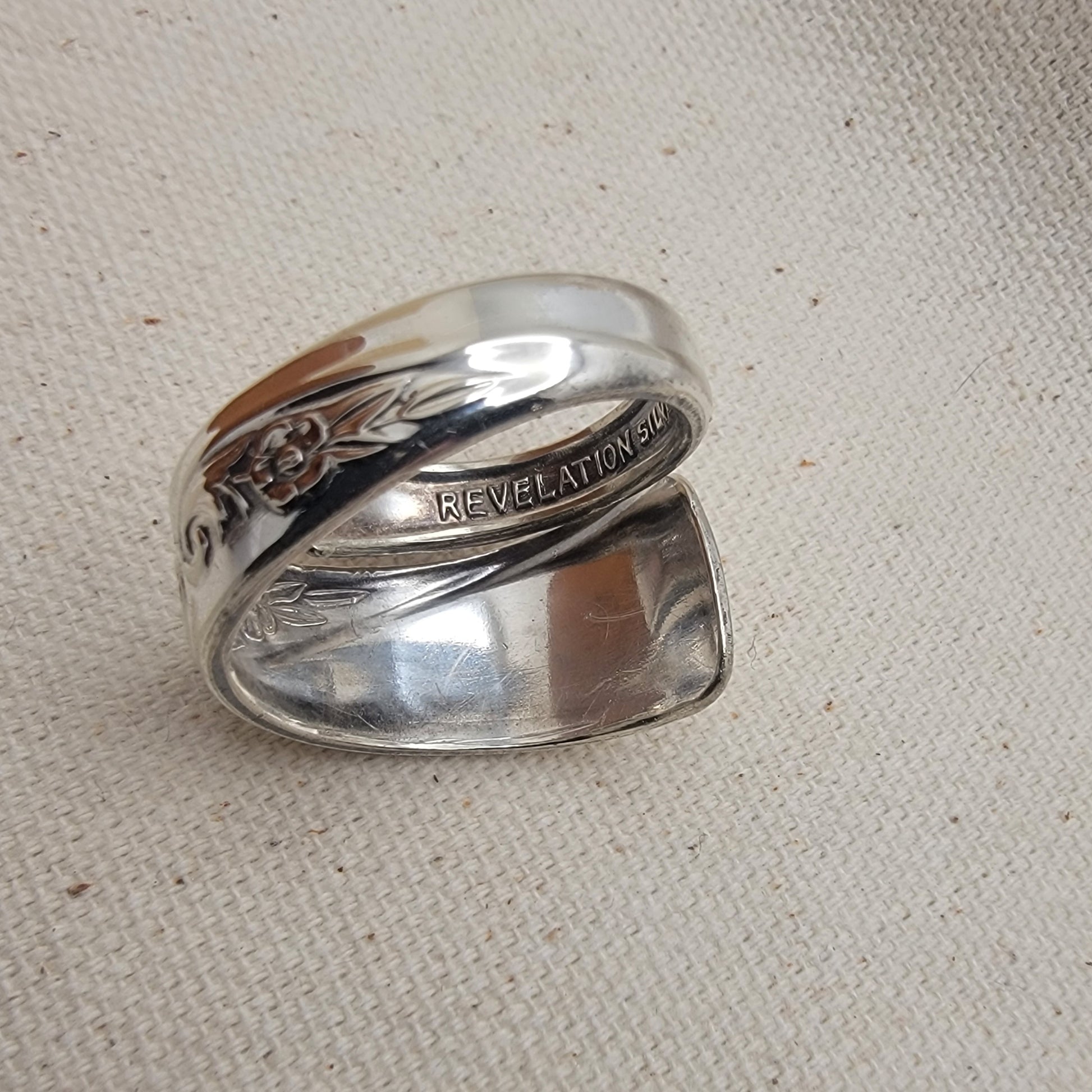 Silver ring with engraved text on a beige fabric background