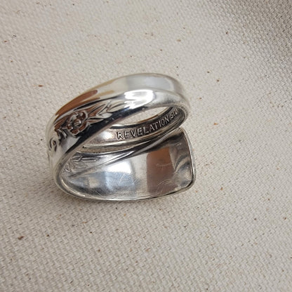 Silver ring with engraved text on a beige fabric background