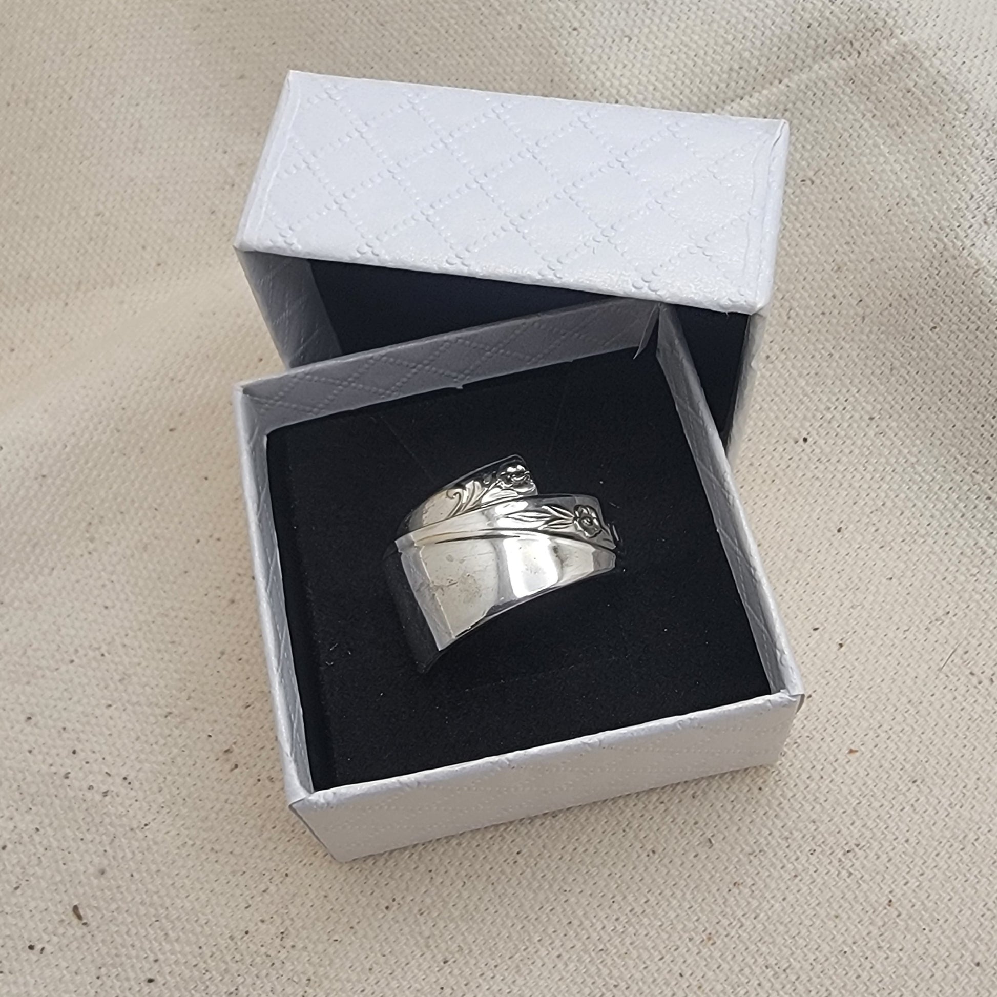 Silver ring in an open white box on a beige fabric background