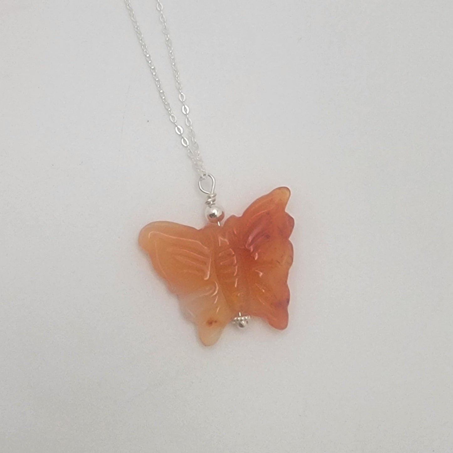 Butterfly-shaped orange gemstone pendant on a chain against a white background