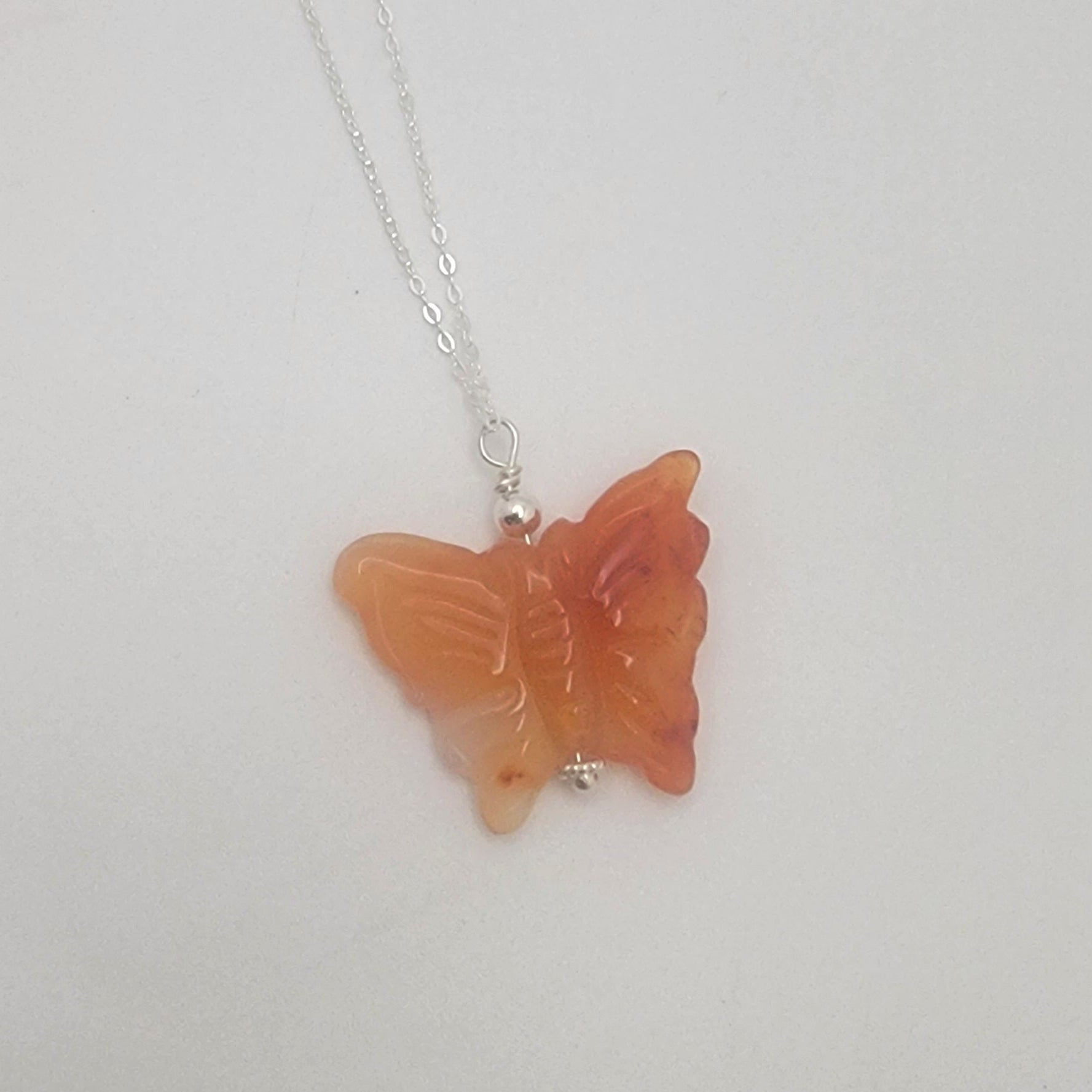 Butterfly-shaped orange gemstone pendant on a chain against a white background