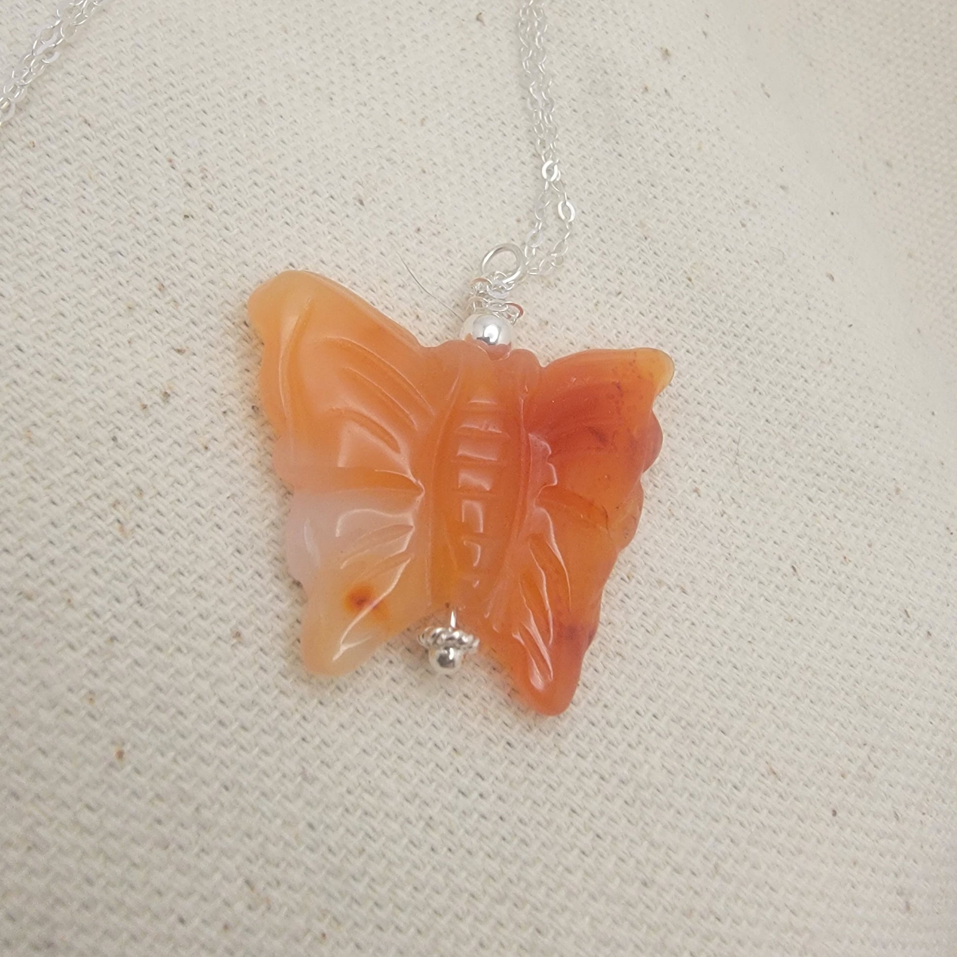 Butterfly-shaped pendant on a chain against a beige fabric background