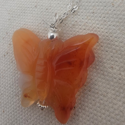 Butterfly-shaped orange pendant on a chain against a textured beige background