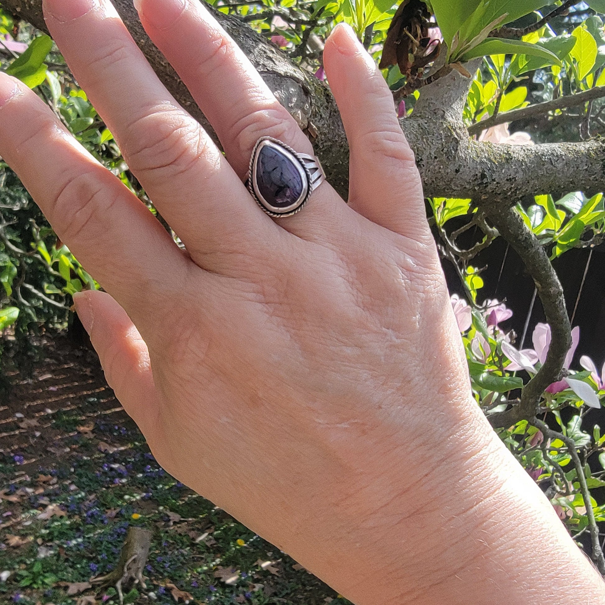 Hand wearing a ring with a purple stone against a natural background