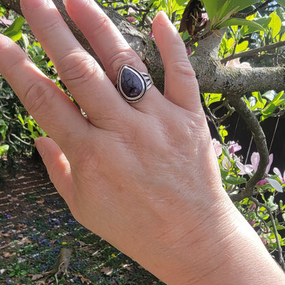 Hand wearing a ring with a purple stone against a natural background