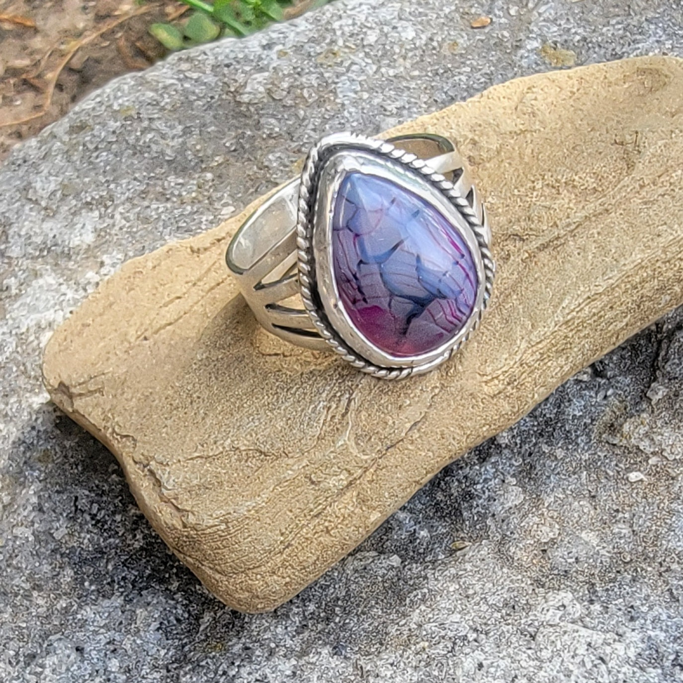 Purple gemstone and sterling silver ring displayed on a stone
