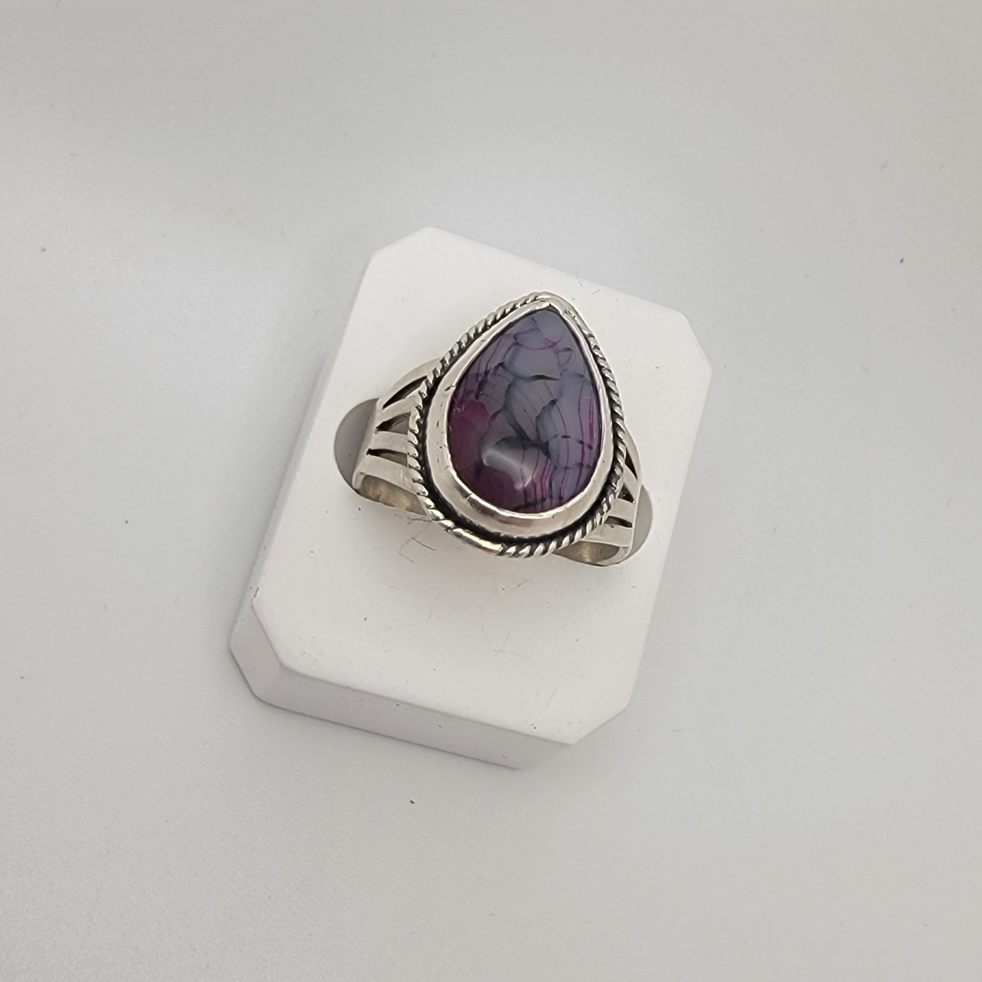Silver ring with a purple stone on a white stand against a light gray background