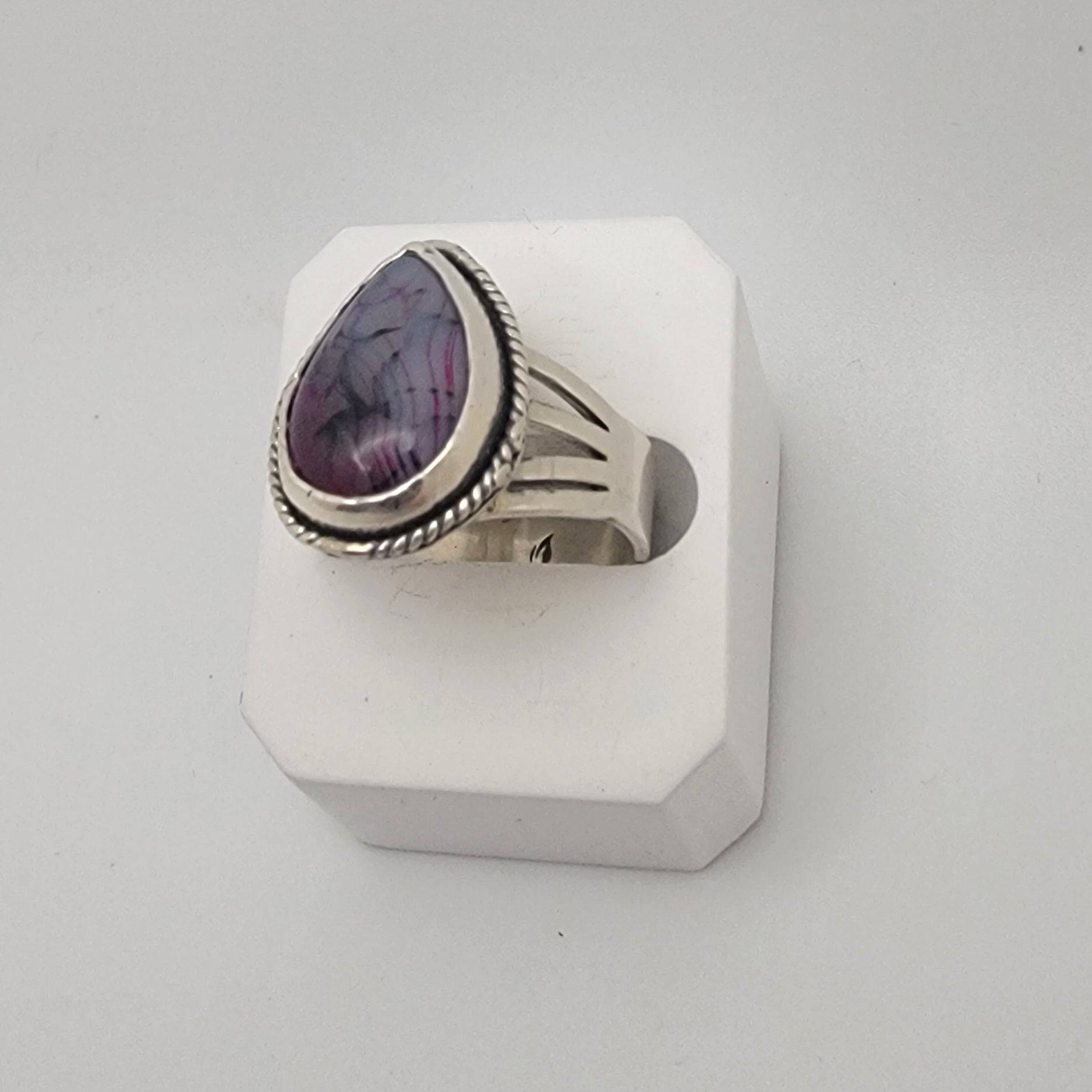 Silver ring with a purple stone on a white stand against a light gray background