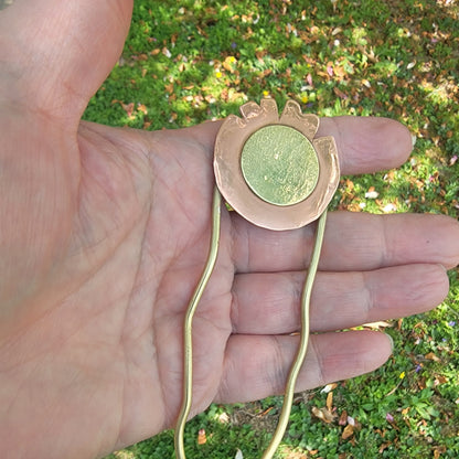 Brass and copper hairpin held in a hand with grass in the background