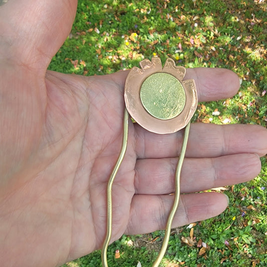 Brass and copper hairpin held in a hand with grass in the background
