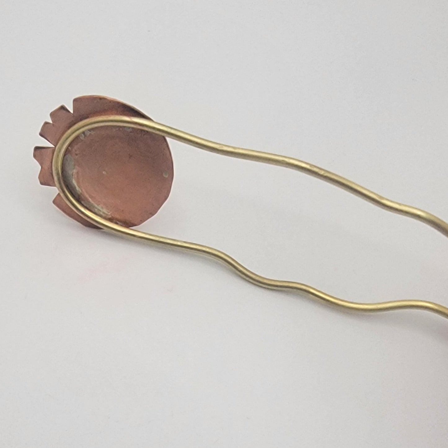 Back of copper and brass hair pin on a light gray background