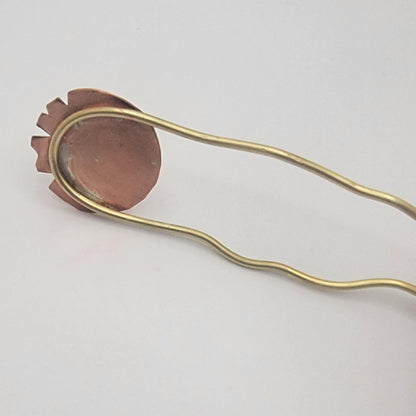 Back of copper and brass hair pin on a light gray background