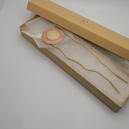 Brass and copper hair pin in a brown box on a light gray background