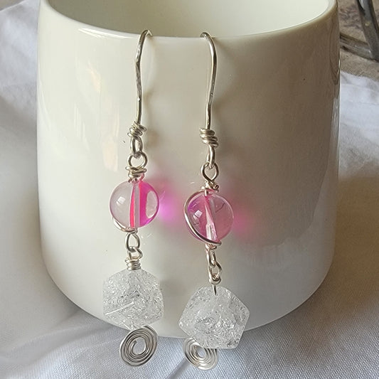 Silver earrings with pink and clear beads hanging in front of a white mug.