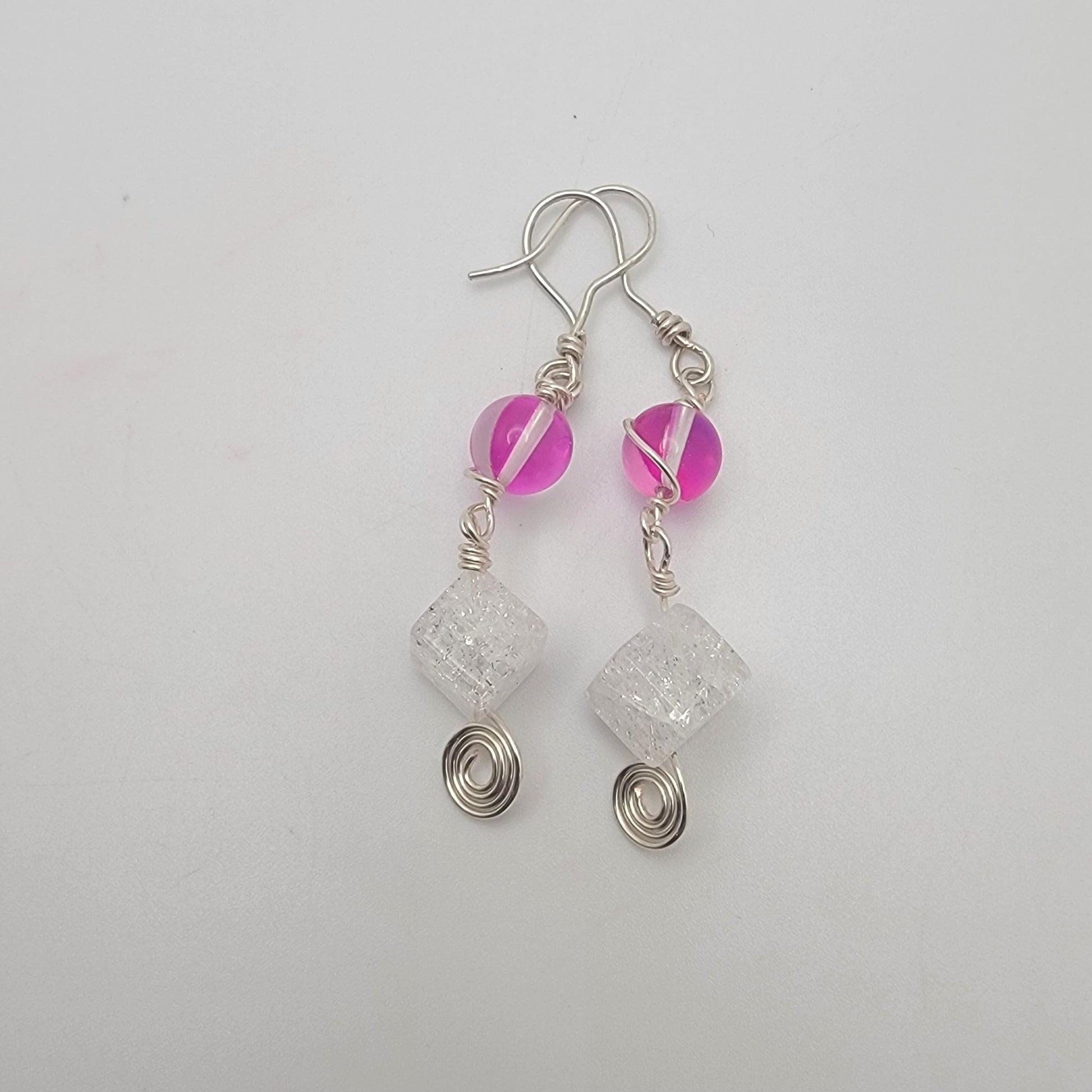 Pair of earrings with pink beads and silver wire on a light gray background