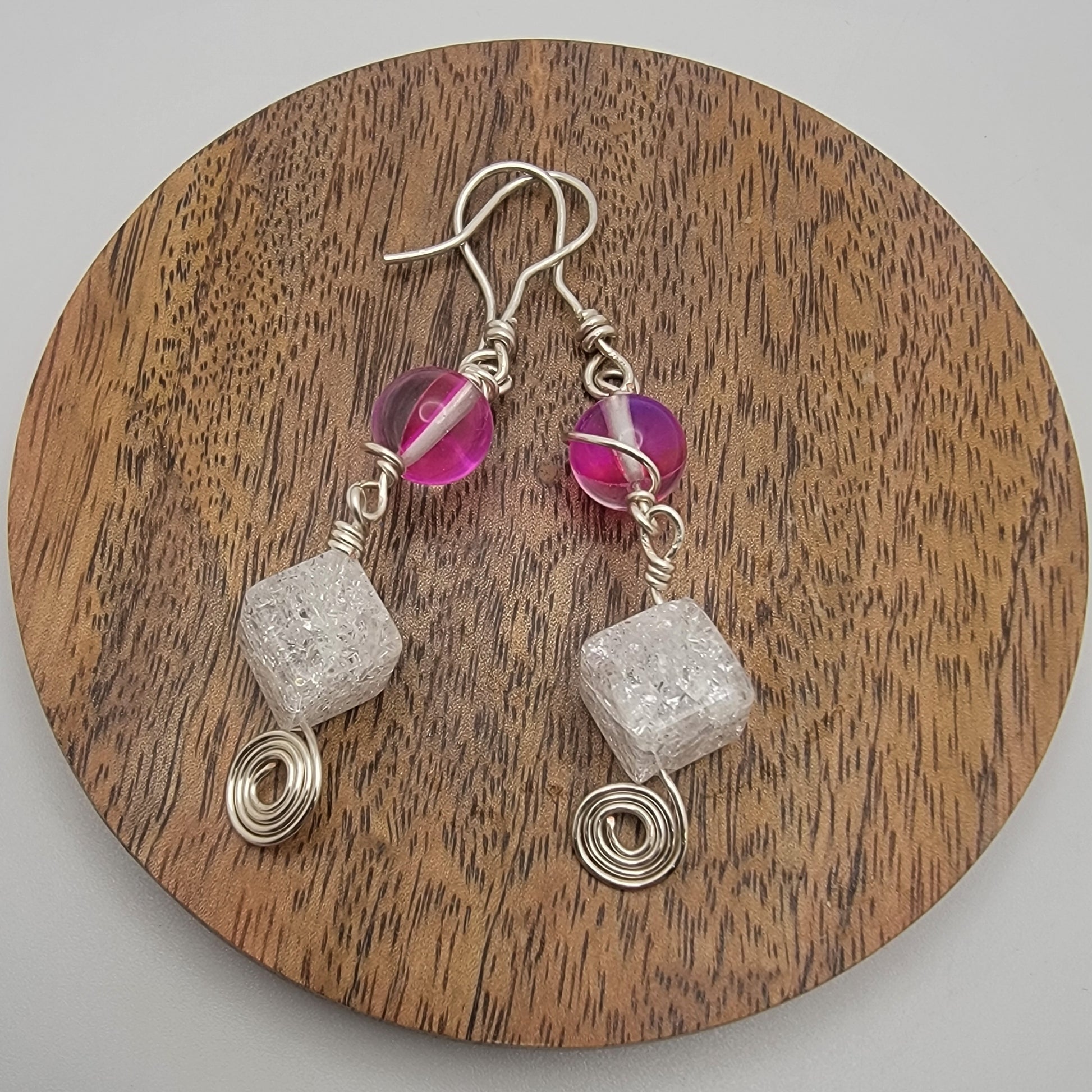 Pair of earrings with pink beads and silver cubes on a wooden board