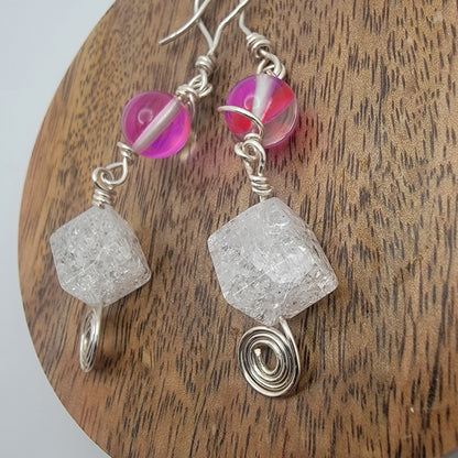 Earrings with pink beads and clear crystal-like stones on a wooden surface