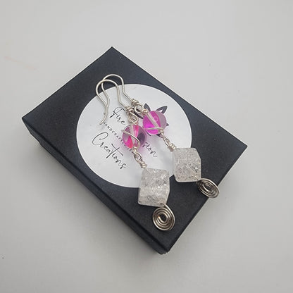 Earrings with pink gemstone and silver wire on a black box with 'The Gemstone Creations' label.