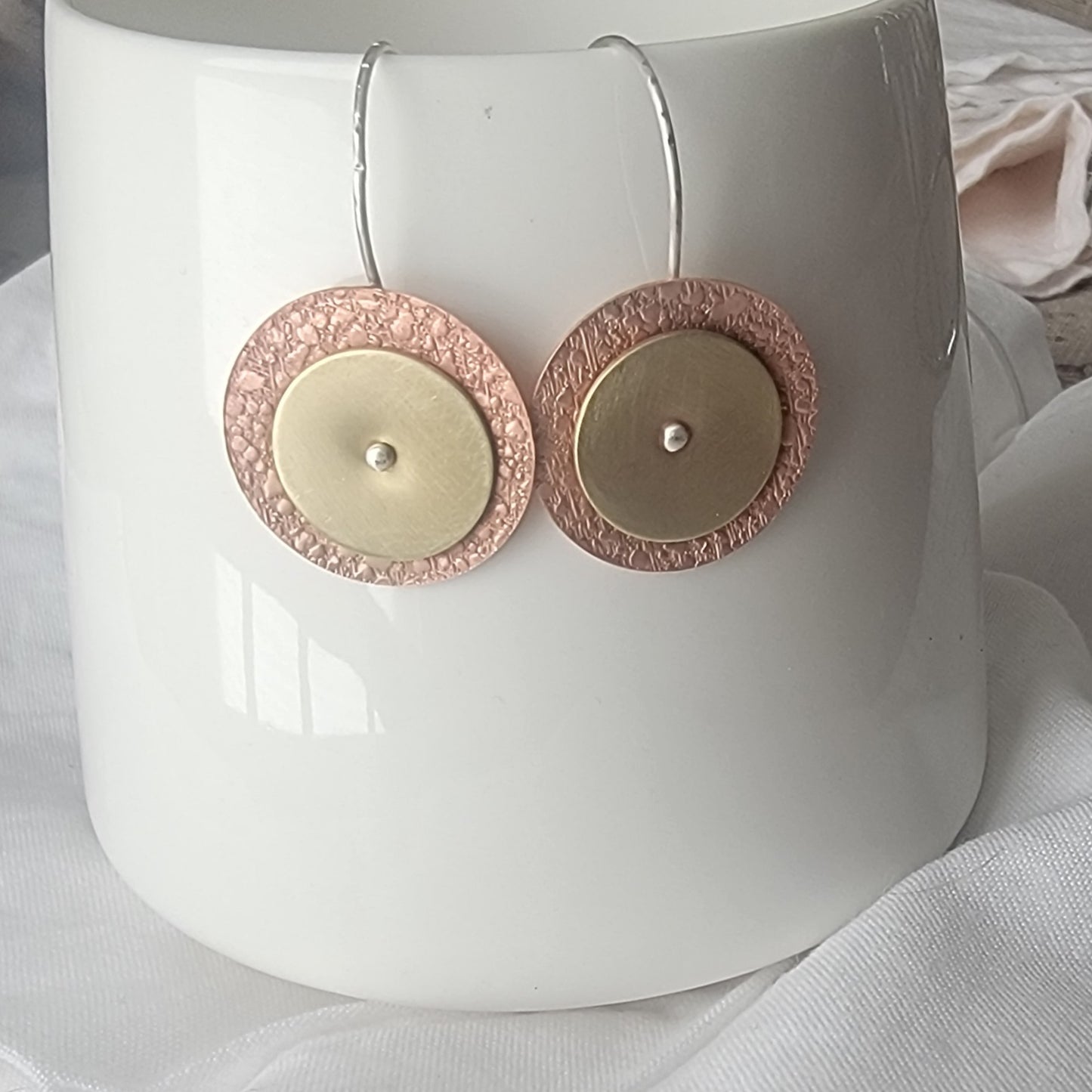 Pair of brass and copper earrings with circular design on a white mug.