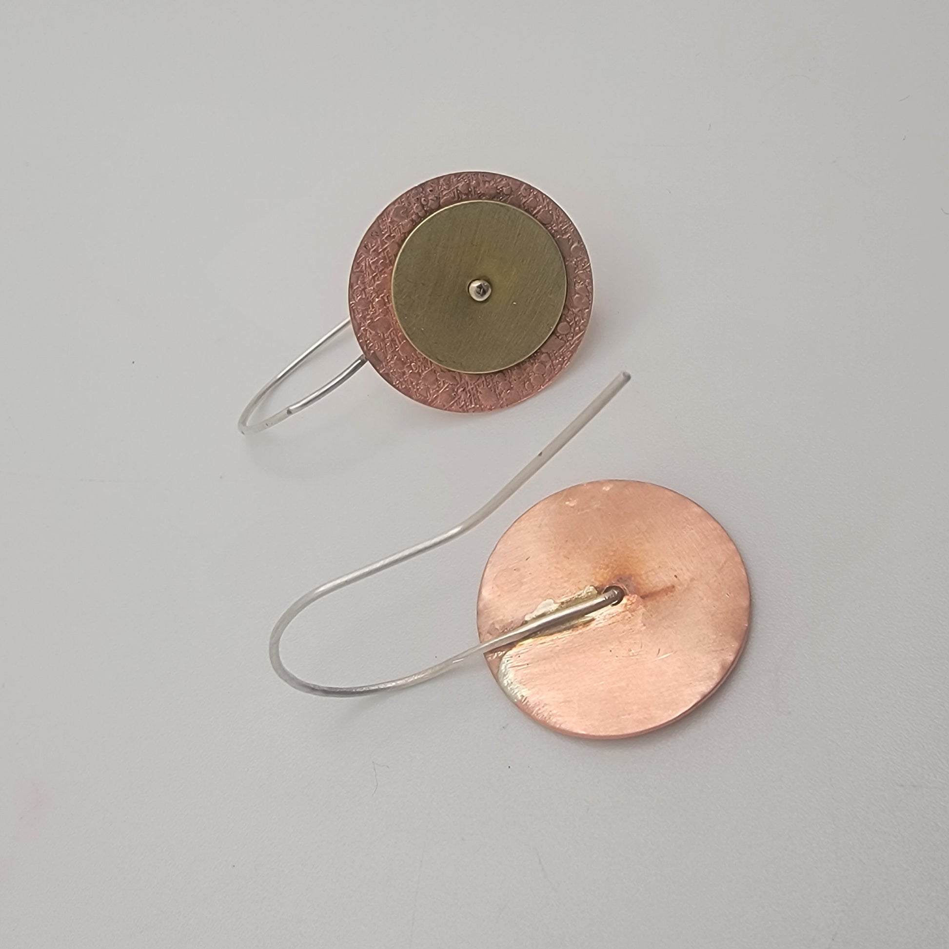 Copper and silver circular earring on a gray background
