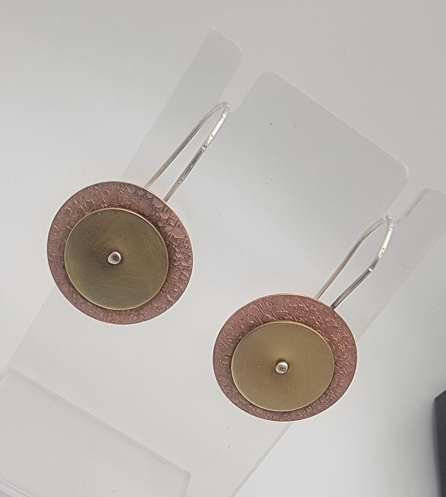 Pair of copper and brass earrings with circular design on a white background