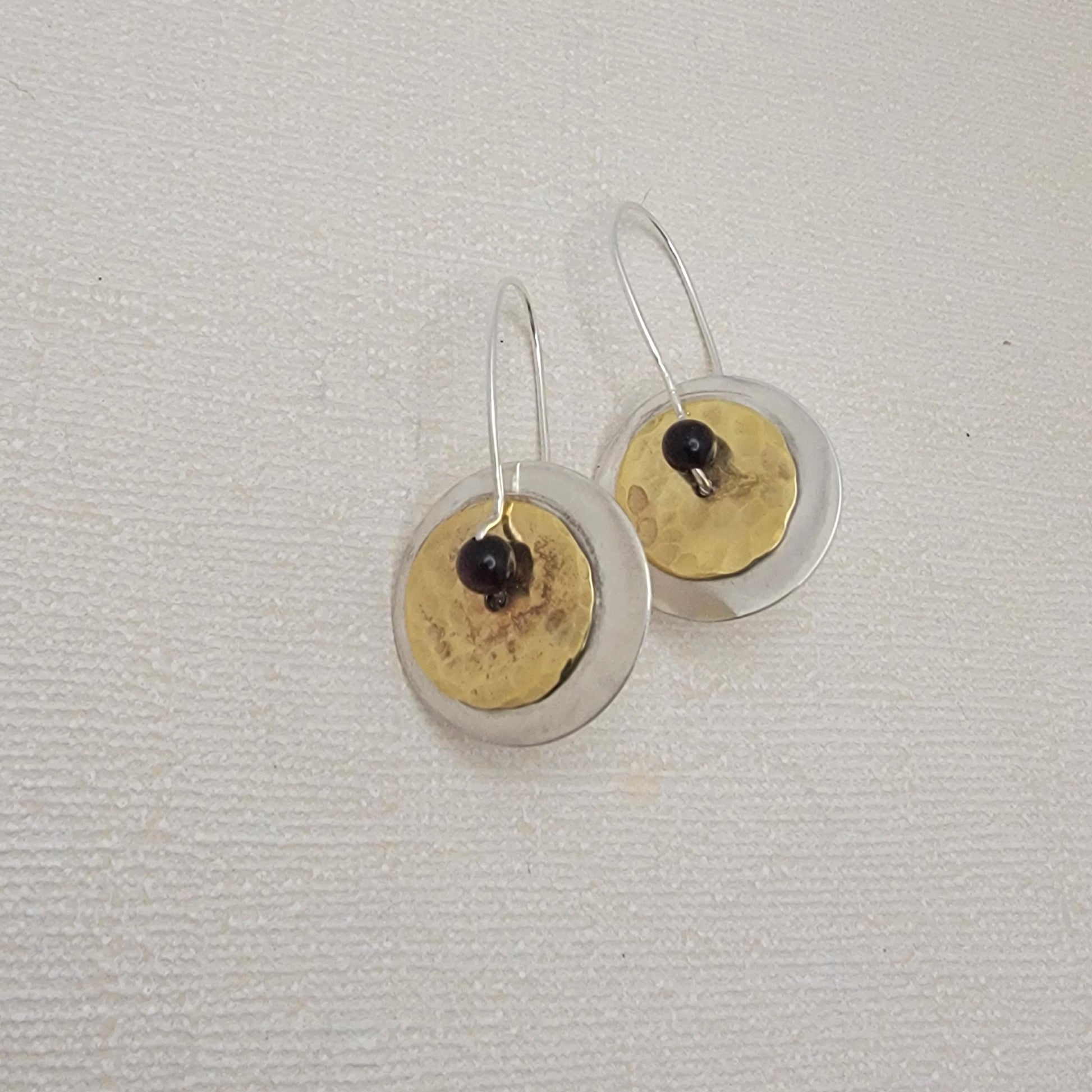 Pair of earrings with hammered brass and silver disc designs on a light gray background