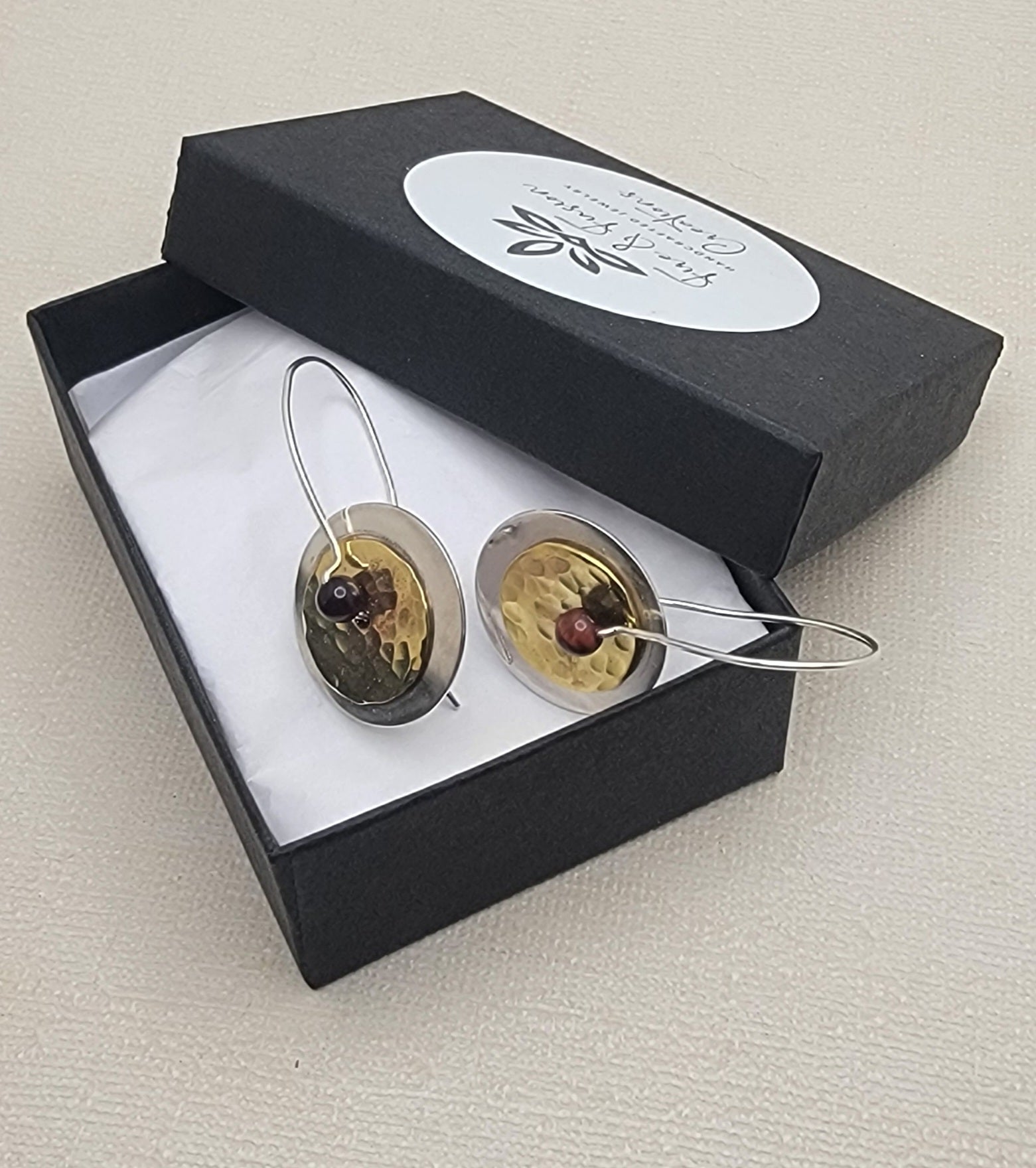 Pair of gold and silver earrings in a black box with a visible brand label.