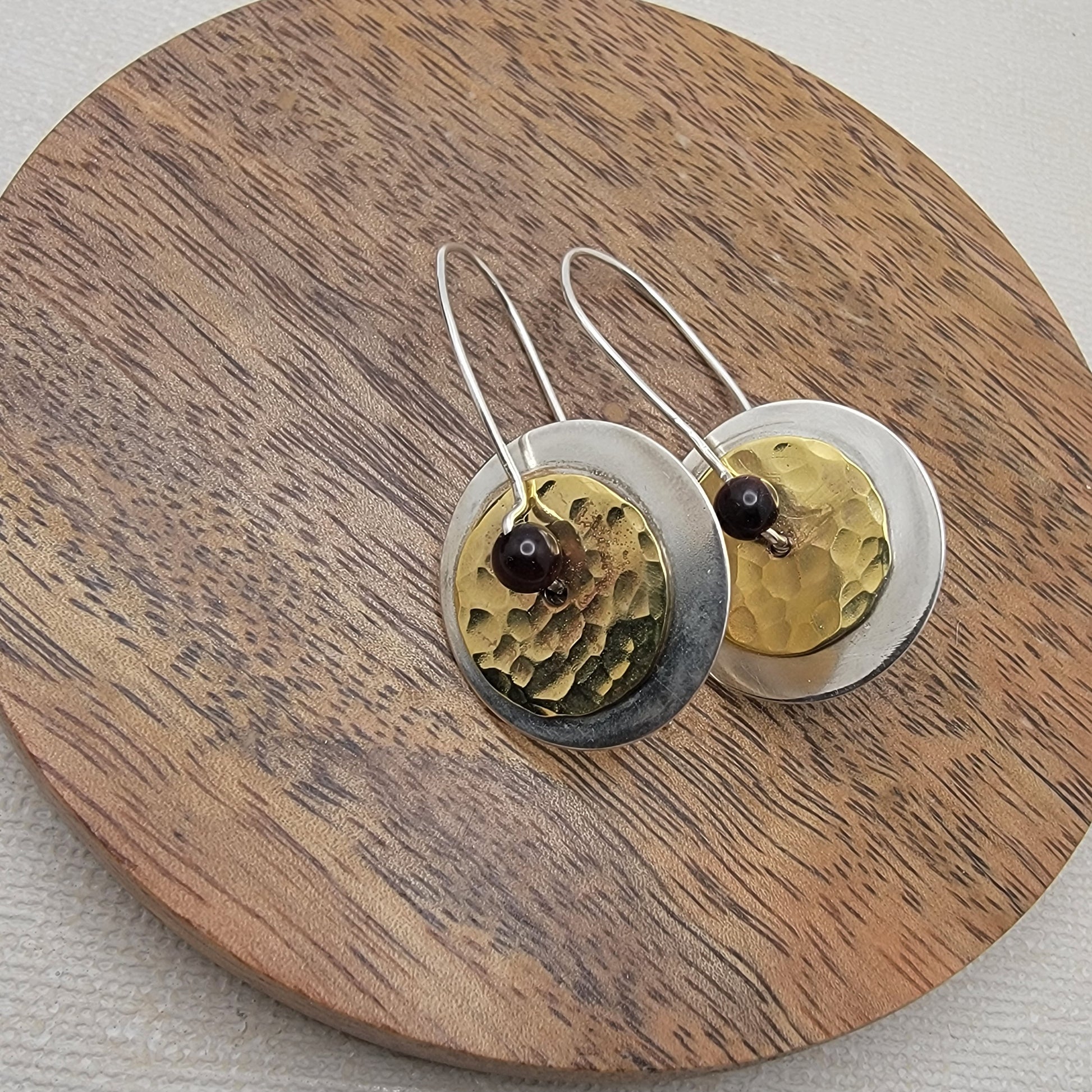 Pair of brass and silver earrings on a wooden surface