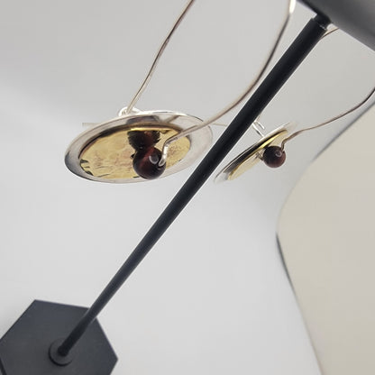 Pair of brass and silver earrings on a stand on a white background
