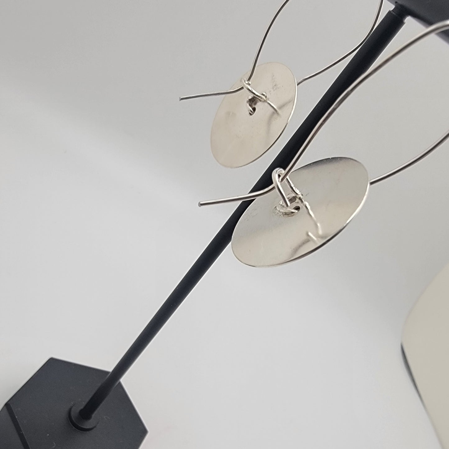 Silver earrings on a black stand against a light gray background