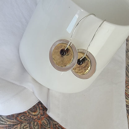 Brass and silver earrings on a white coffee mug with a patterned fabric background