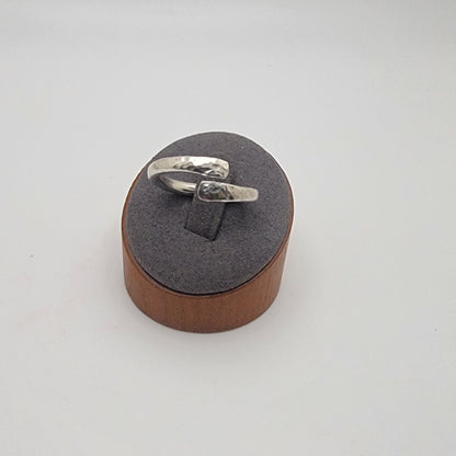 Silver ring on a wooden and gray cushioned stand against a light gray background