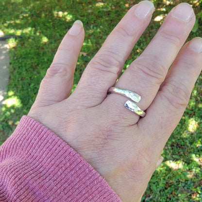 Hand wearing a silver ring with a blurred green outdoor background