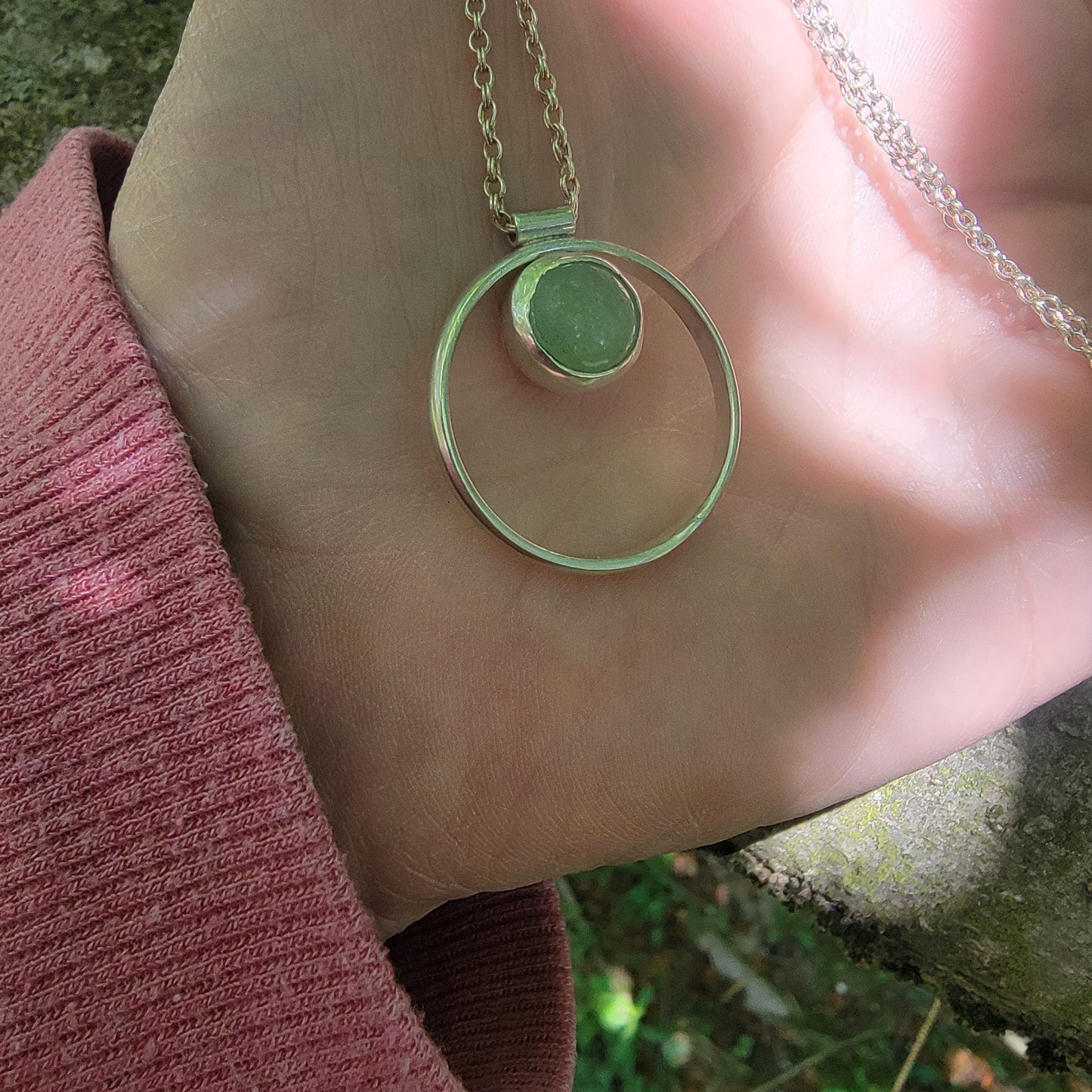 Necklace with a green pendant held in a hand against a natural background