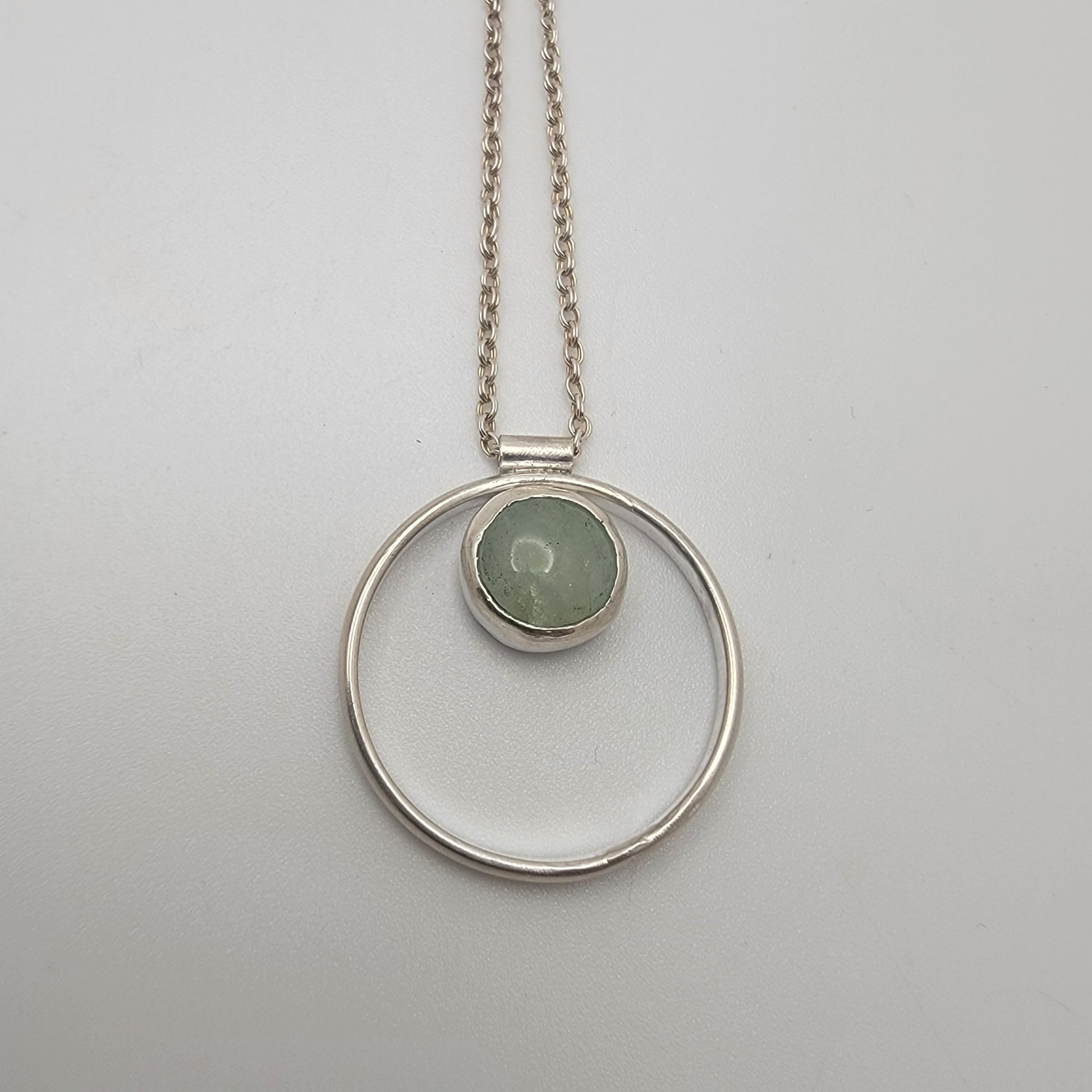 Silver necklace with a circular pendant featuring a green gemstone on a light gray background
