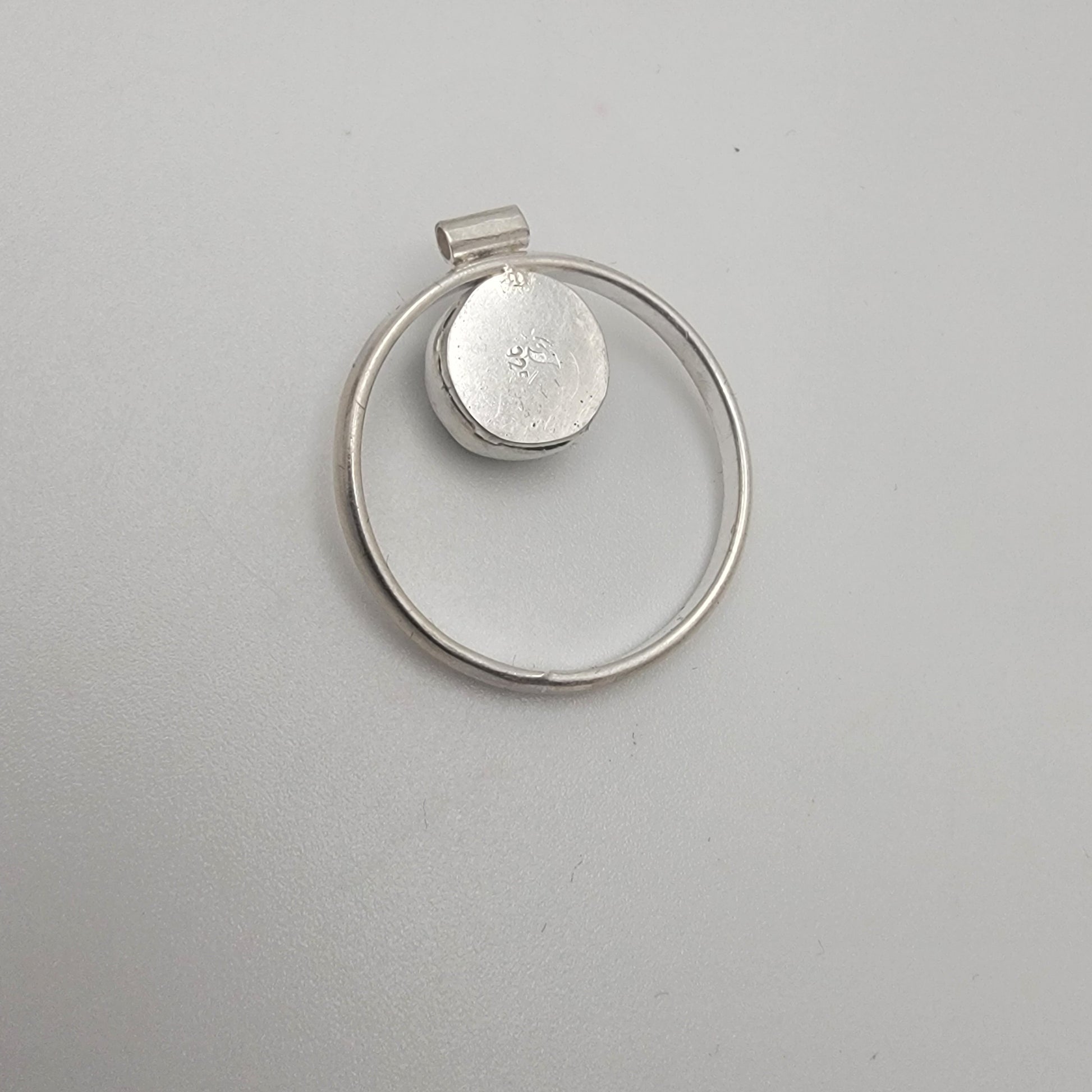 Silver pendant with circular design on a gray background