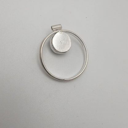 Silver pendant with circular design on a gray background