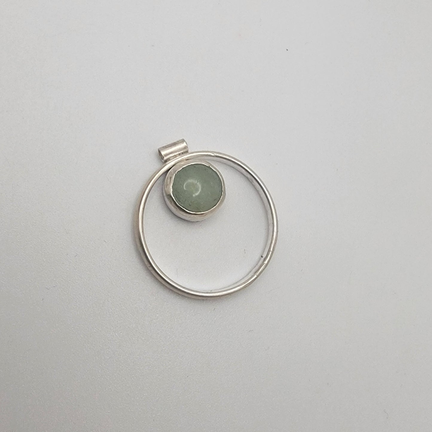 Silver pendant with a green stone on a light gray background