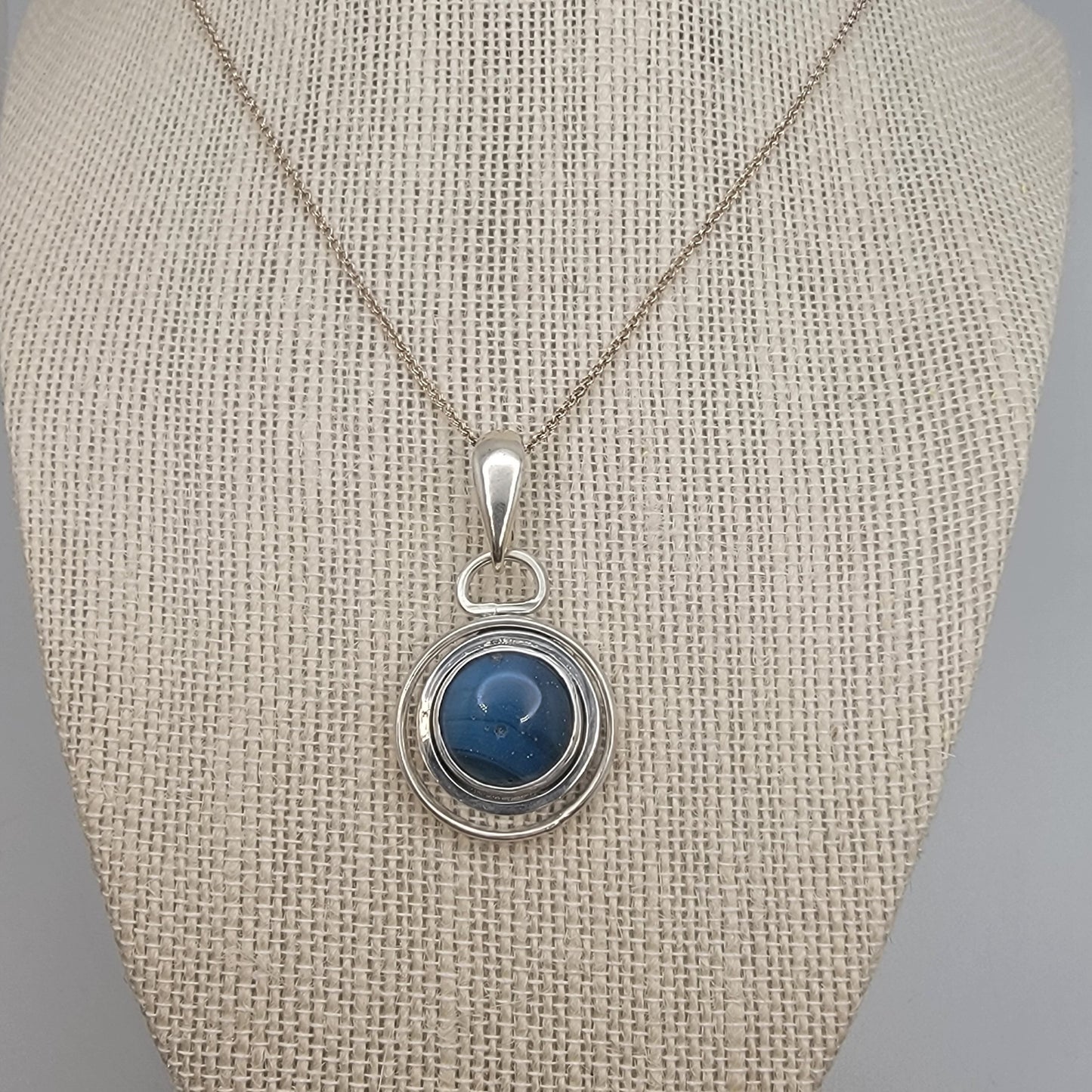 Blue Stone set in sterling silver circular pendant on Sterling Silver chain on beige necklace display