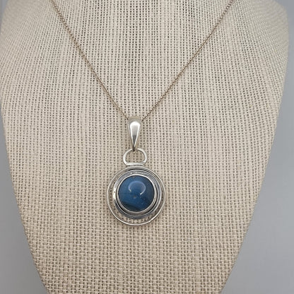 Blue Stone set in sterling silver circular pendant on Sterling Silver chain on beige necklace display