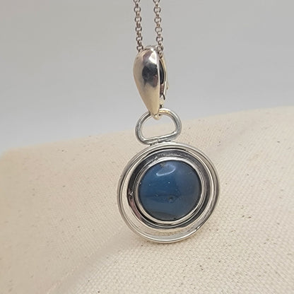 Blue Stone set in sterling silver circular pendant on Sterling Silver chain on beige and white background
