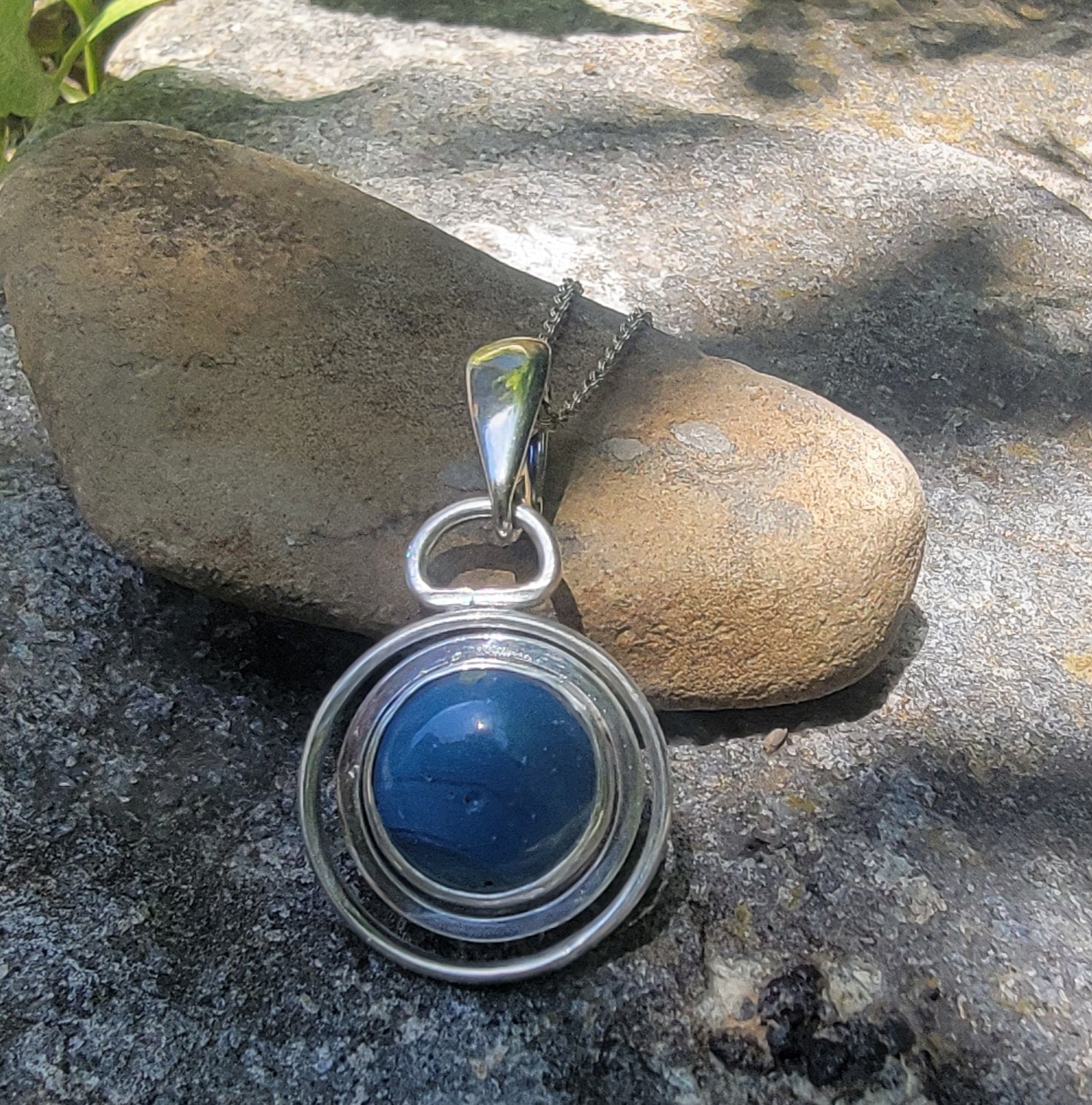 Blue Stone set in sterling silver circular pendant on Sterling Silver chain on light brown stone