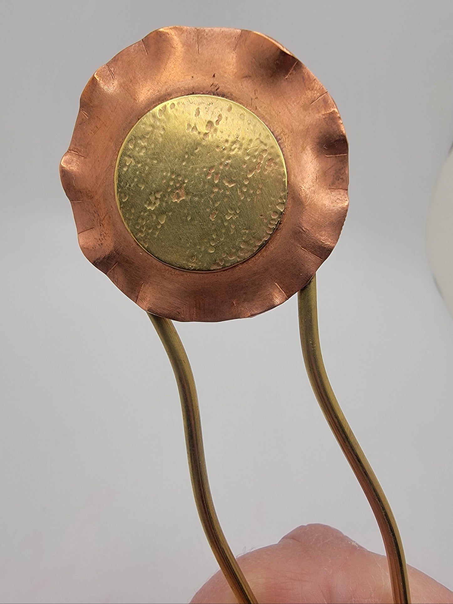 Copper and brass ladle held by a hand against a light gray background