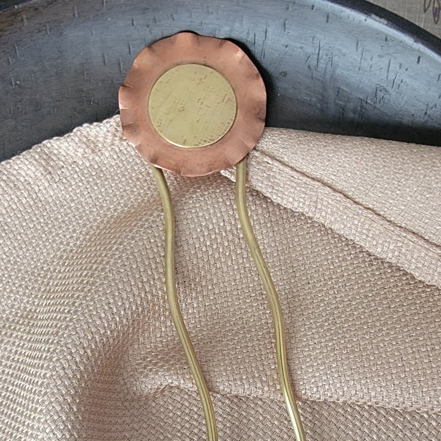 Copper and brass hair clip on a textured fabric background