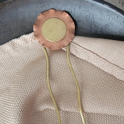 Copper and brass hair clip on a textured fabric background