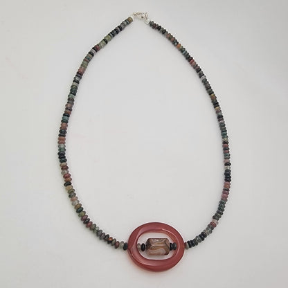 Beaded necklace with small earth tone beads and large oval carnelian bead on a white background