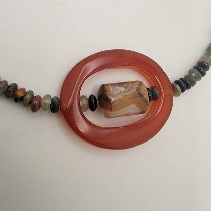 Close up view of a beaded necklace with small earth tone beads and large oval carnelian bead on a white background
