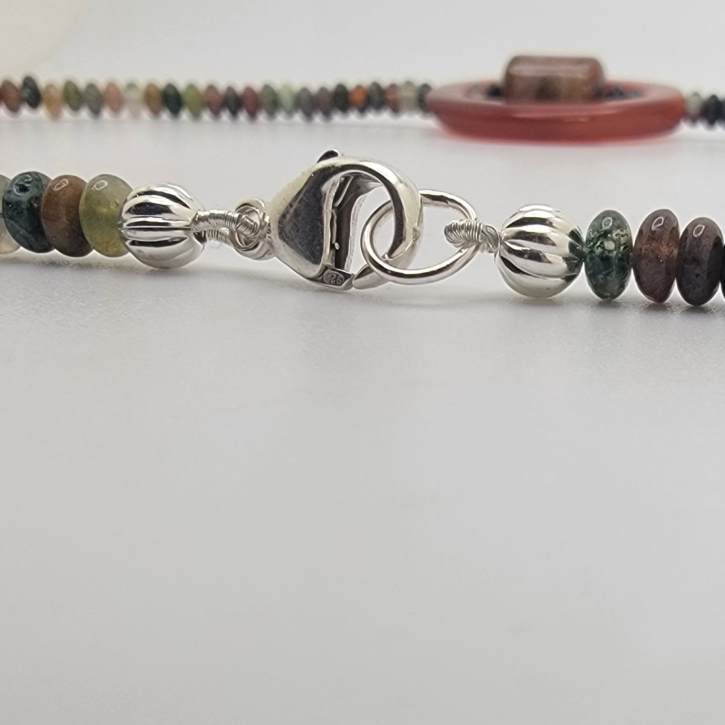 Close up view of a silver lobster clasp on a beaded necklace on a white background