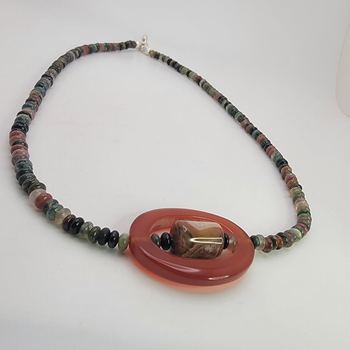 Beaded necklace with small earth tone beads and large oval carnelian bead on a white background