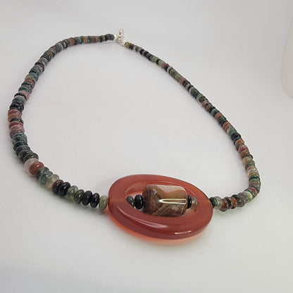Beaded necklace with small earth tone beads and large oval carnelian bead on a white background